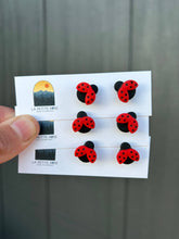 Load image into Gallery viewer, Hand holding red and black ladybug clay stud earrings on display cards.