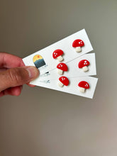 Load image into Gallery viewer, Hand holding cards of red and white mushroom clay stud earrings.