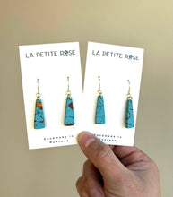 Load image into Gallery viewer, Hand holding two pairs of marbled turquoise-colored clay dangle earrings.

