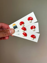 Load image into Gallery viewer, Red mushroom clay stud earrings arranged on three white display cards.
