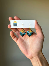 Load image into Gallery viewer, Hand holding a pair of peacock-inspired clay hoop earrings.
